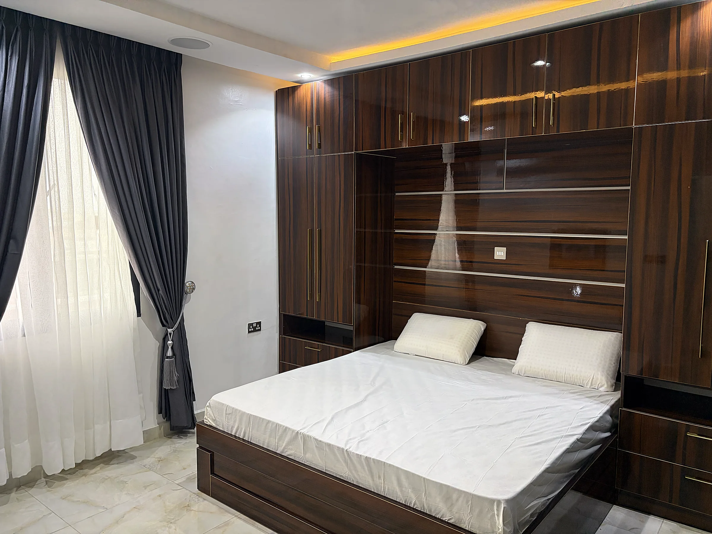 Second bedroom with dark timber fitted storage, bedside cabinetry and full-height curtains